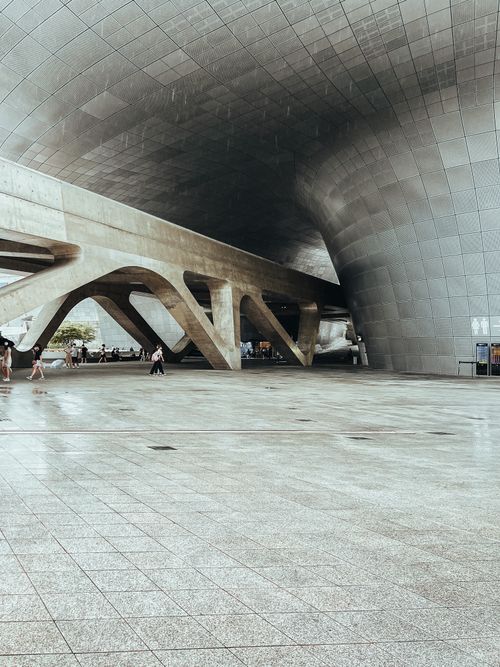 Free Wide-angle view of a futuristic architectural space with people walking, featuring unique curved design and open space. Stock Photo