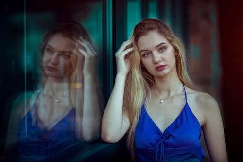 Woman in Blue Dress Standing Near Glass Window