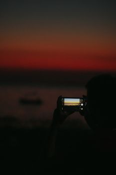 Silhouette of a person taking a sunset photo in Toroni, Greece.