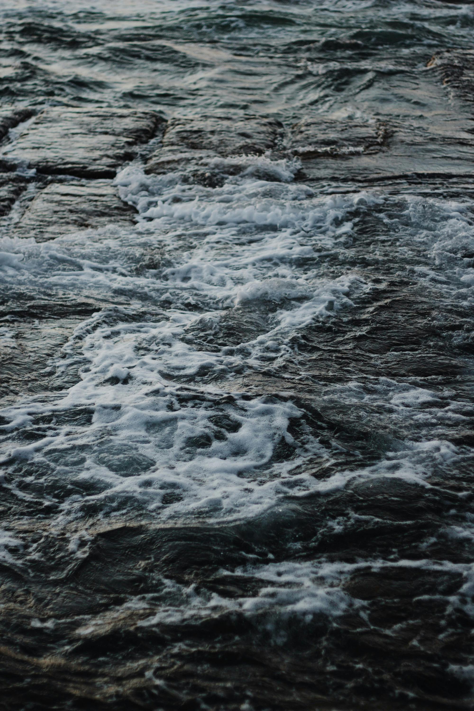 Close-up of waves crashing on rocks with sea foam and strong currents.