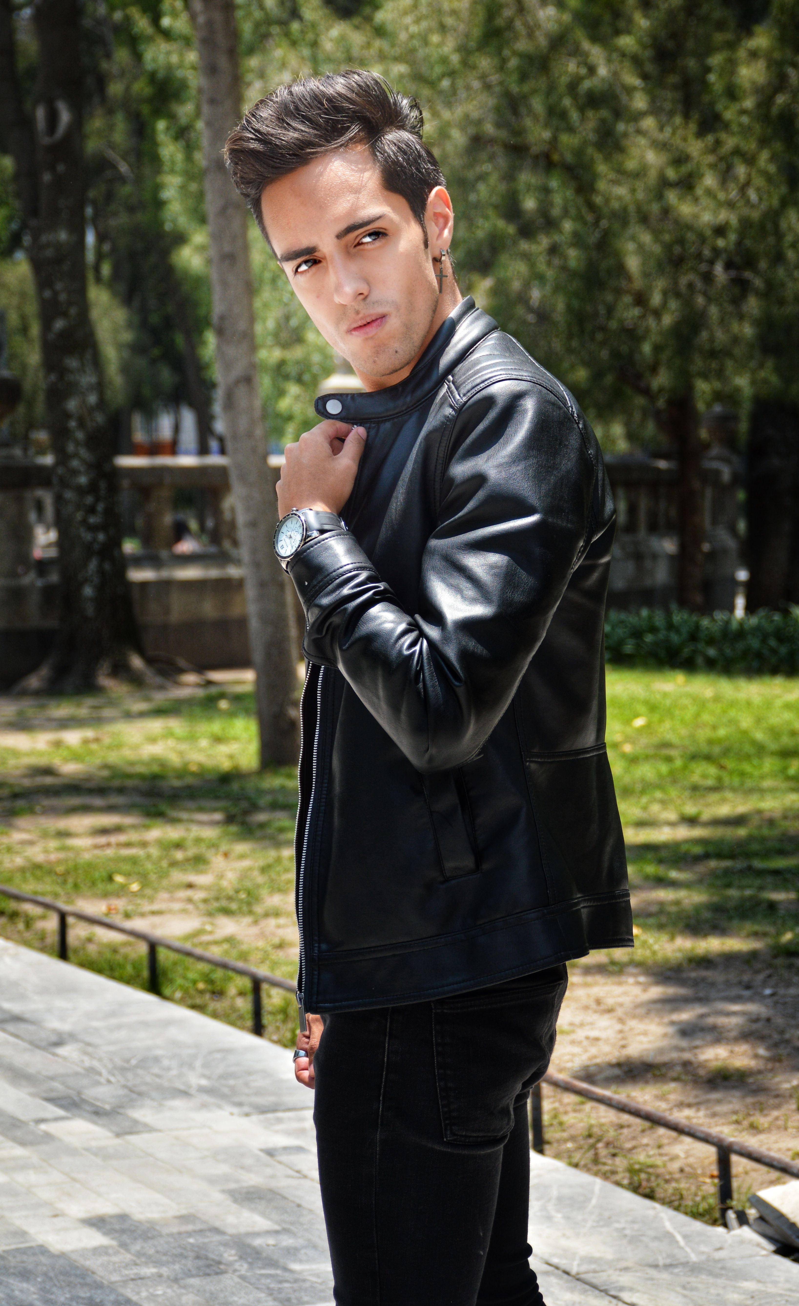 Fashionable man striking a pose in Mexico City park wearing a black leather jacket.