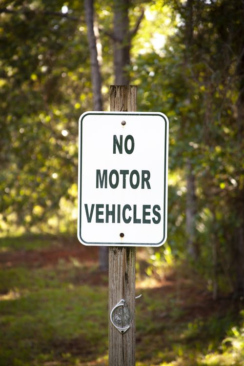 Free A wooden post with a 'No Motor Vehicles' sign against a forest backdrop. Stock Photo