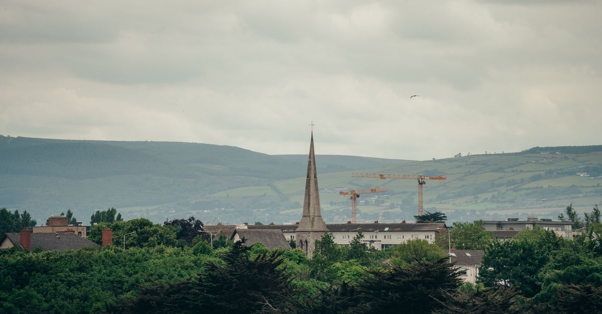 Scenic urban landscape featuring a church spire and lush greenery against a backdrop of rolling hills.