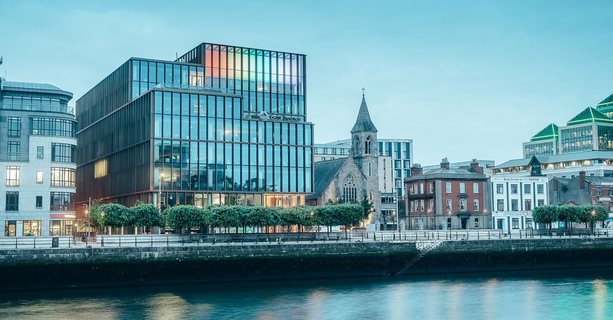 A vibrant cityscape featuring modern glass buildings along a tranquil riverfront in a bustling urban environment.