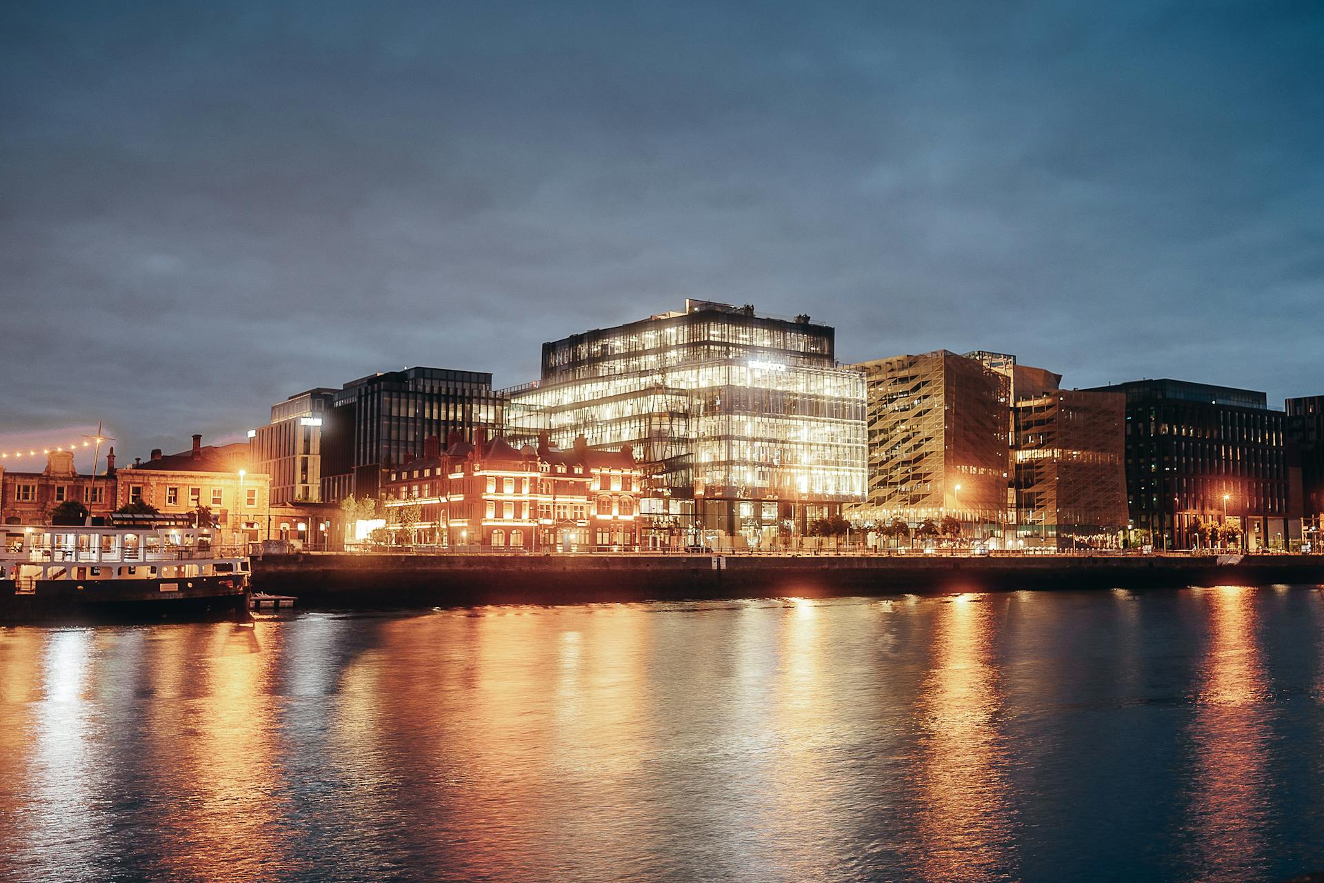 Illuminated modern buildings along Dublin riverside reflecting on water at night.