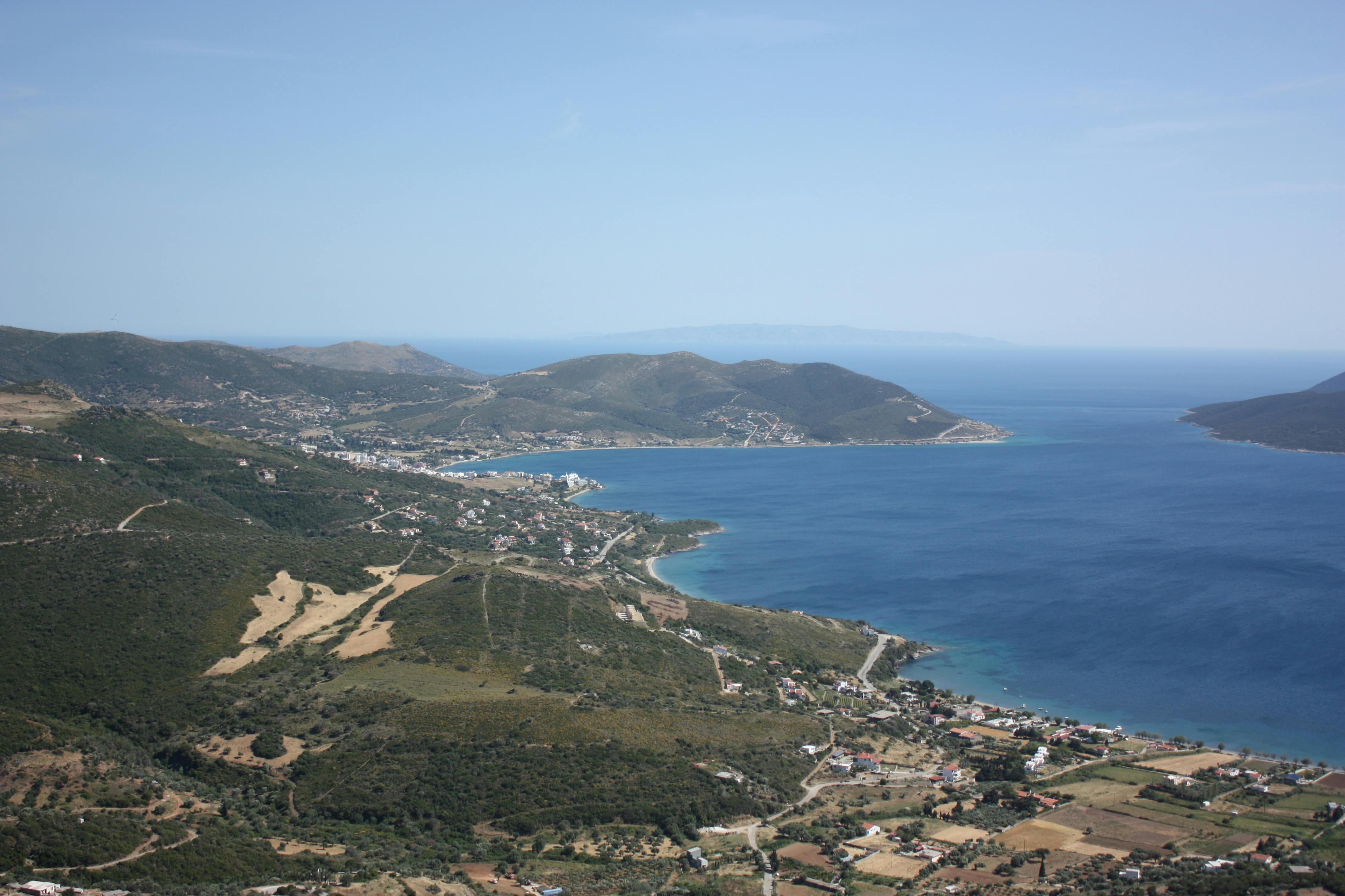 Serene aerial view of a coastal landscape with lush hills and turquoise waters under a clear blue sky.