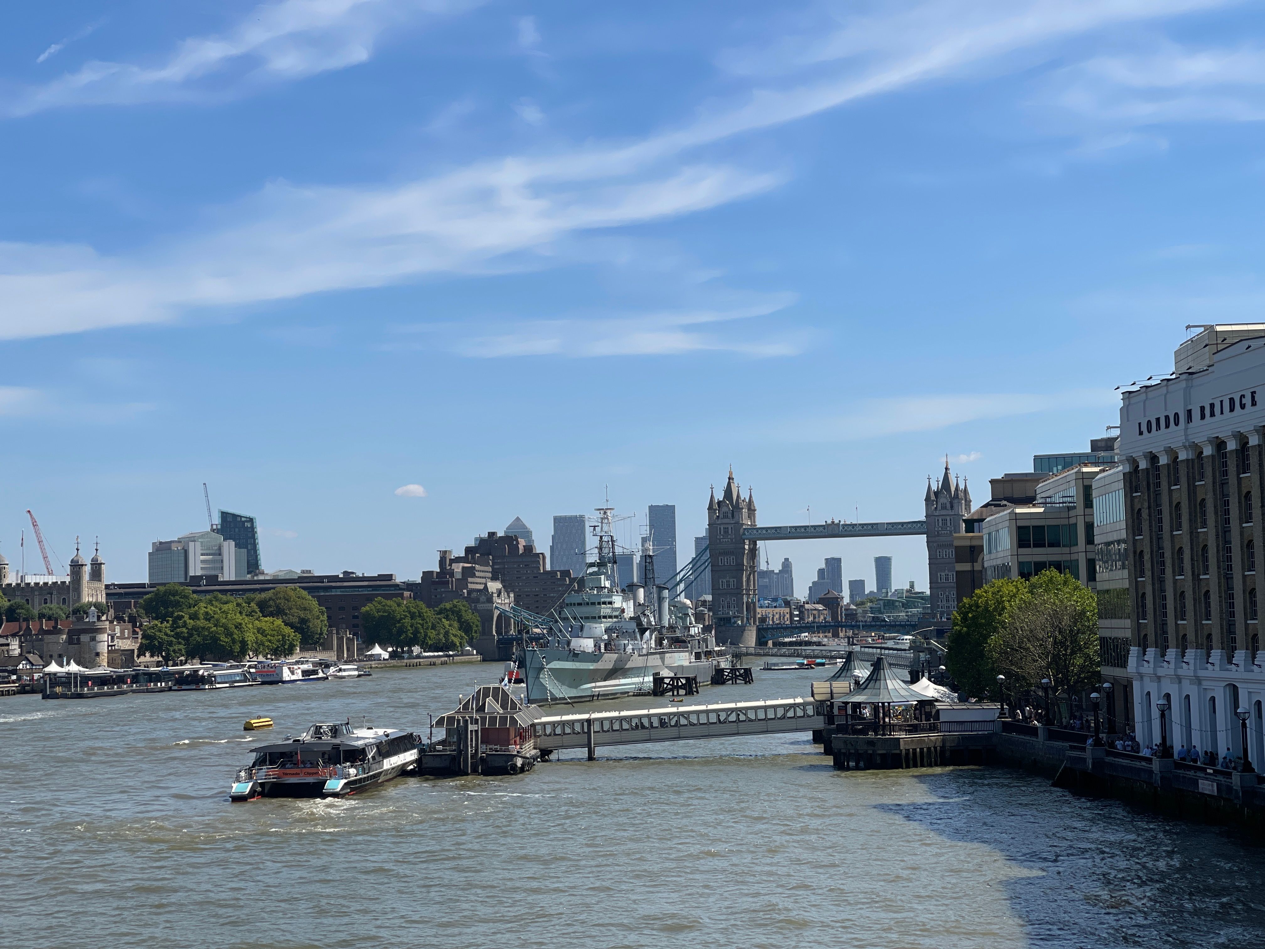 Scenic view of Tower Bridge, Thames River, and cityscape in London under a clear blue sky.