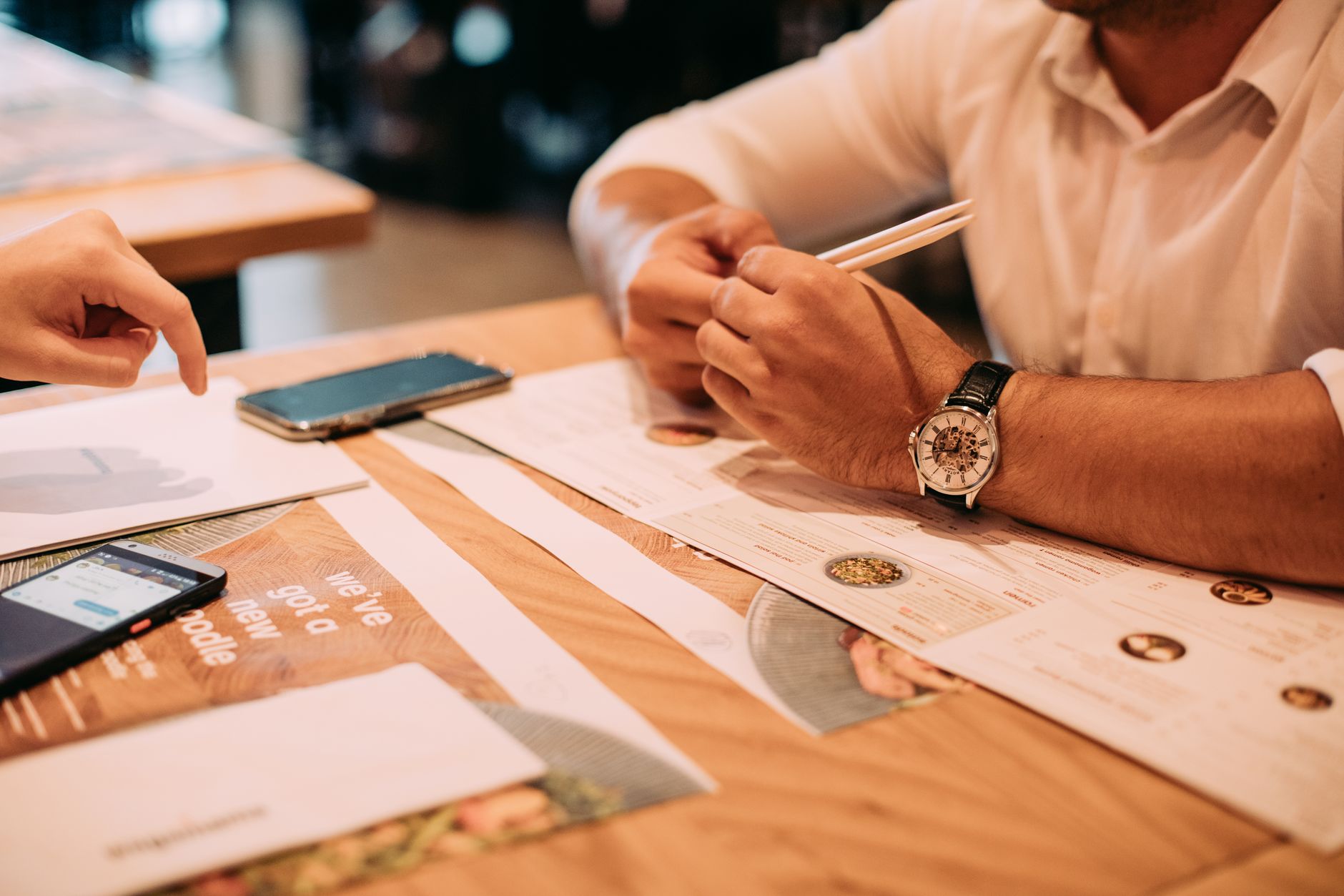 手機離線翻譯相機模式:招牌菜單快速讀的實用指南 Two adults discussing a menu at a restaurant table with chopsticks and phones.