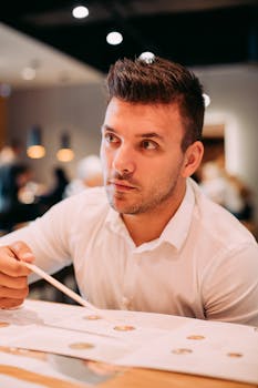 A man reads a menu at a restaurant table, captured in a candid moment.