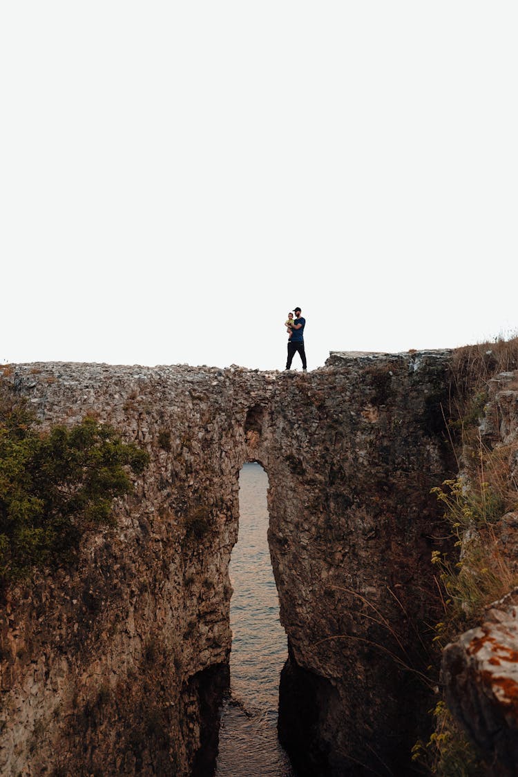 Man Holding A Baby On A Cliff 