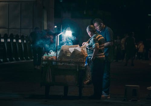A Man Selling Food on the Street During Night Time 