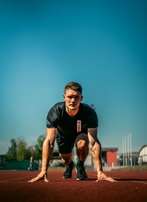 Fit male athlete on track getting ready to sprint under clear blue sky. Fit male athlete on track getting ready to sprint under clear blue sky.