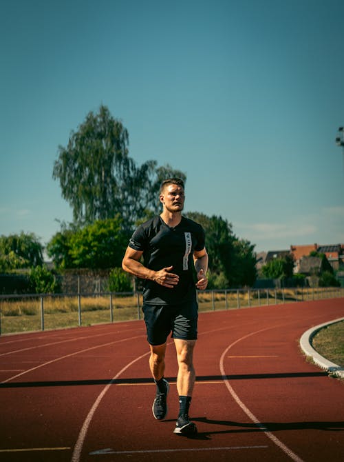 A Man in Black Shirt Running on the Track Field