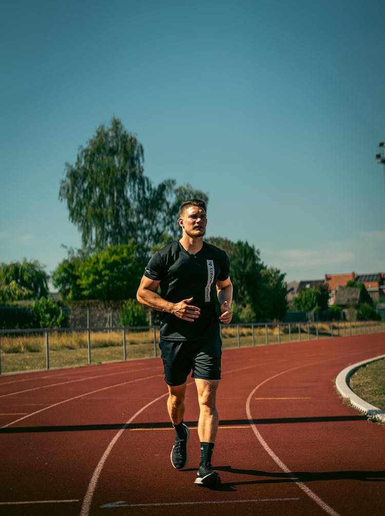 A Man In Black Shirt Running On The Track Field