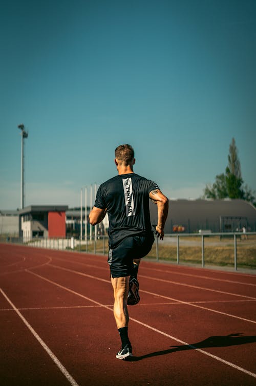 A Back View of a Man in Black Shirt Running on the Track Field