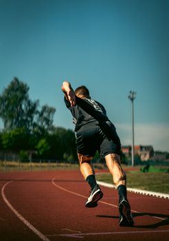 Athletic man sprinting on a sunny day at a running track in Andenne, Belgium.