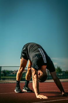 Man stretching on a running track, preparing for athletic training in Andenne, Belgium.