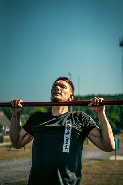 Athletic man in black shirt doing pull-ups on a metal bar outdoors under blue sky for fitness and strength. Athletic man in black shirt doing pull-ups on a metal bar outdoors under blue sky for fitness and strength.