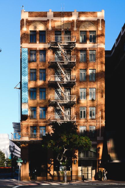 A classic urban building with fire escape stands out in the city, bathed in warm sunlight.