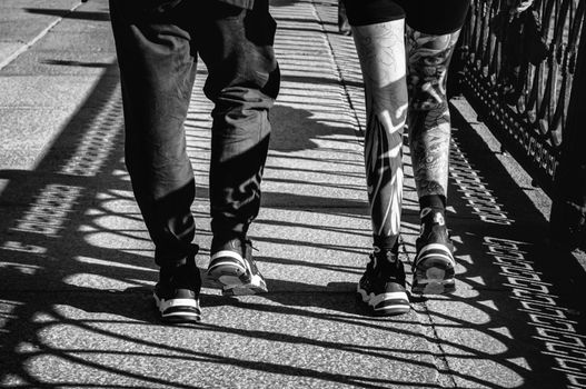 Two people walking with tattooed legs, captured in black and white shadows.