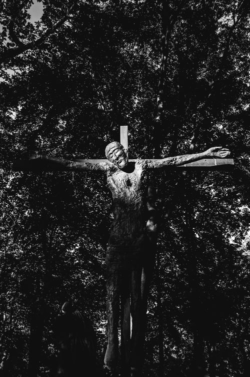 Free Monochrome image of a crucifix sculpture amidst trees, showcasing sacred art outdoors. Stock Photo