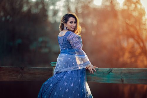 Free A woman in a blue traditional dress smiles gracefully outdoors at sunset, embracing cultural elegance. Stock Photo