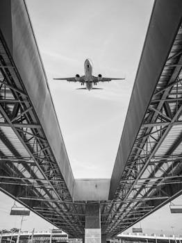 A black and white image of an airplane flying over urban structures, creating a dramatic visual contrast.