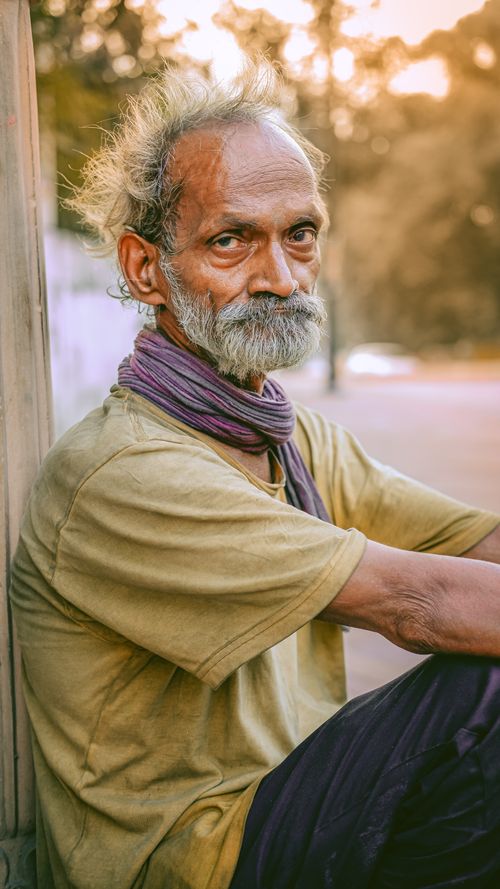 Free Close-up portrait of a contemplative elderly man with beard sitting outdoors in soft lighting. Stock Photo
