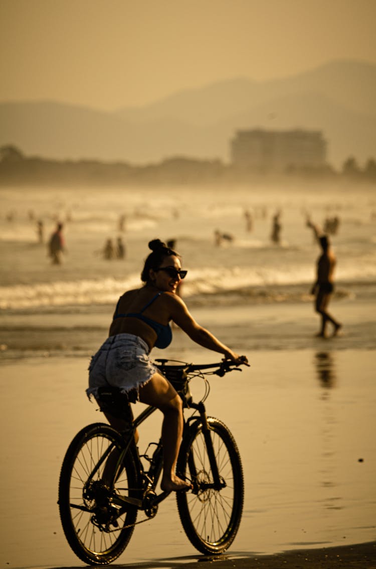 A Woman In Denim Shorts Riding A Bicycle On The Beach