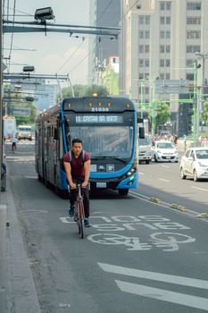 A cyclist rides ahead of a bus in a bustling city street, showcasing urban transportation dynamics.
