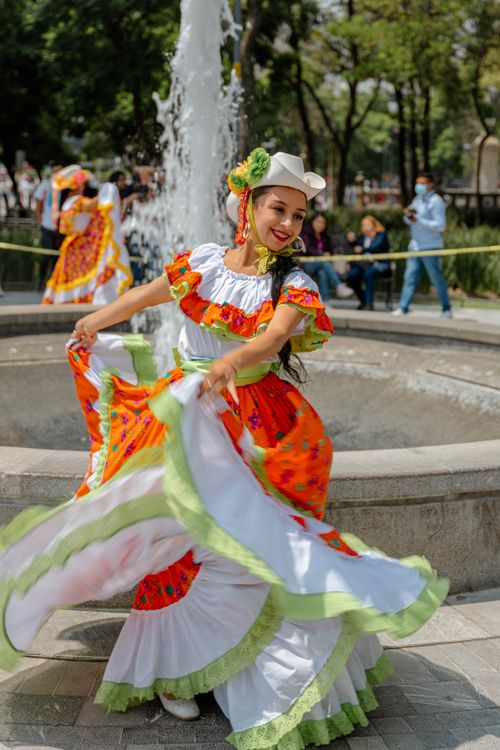 Free Festive Mexican dancer in traditional dress performing by a fountain, radiating joy and culture. Stock Photo