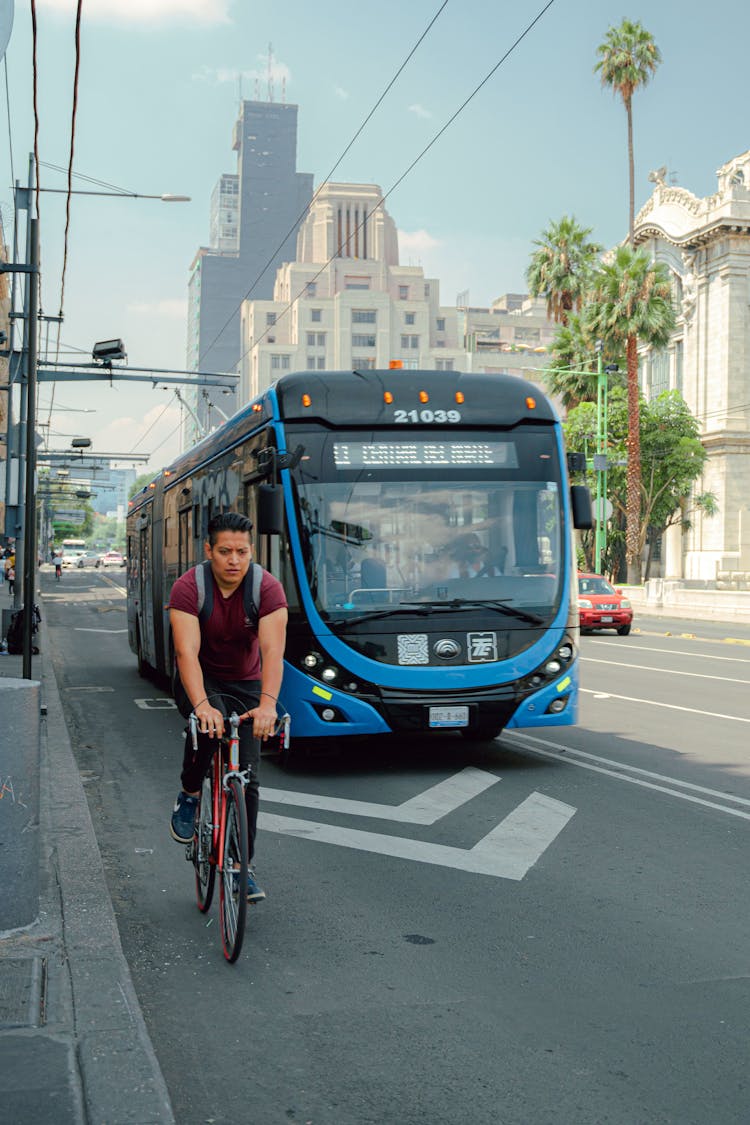 A Man Riding A Bike On The Road Near The Bus