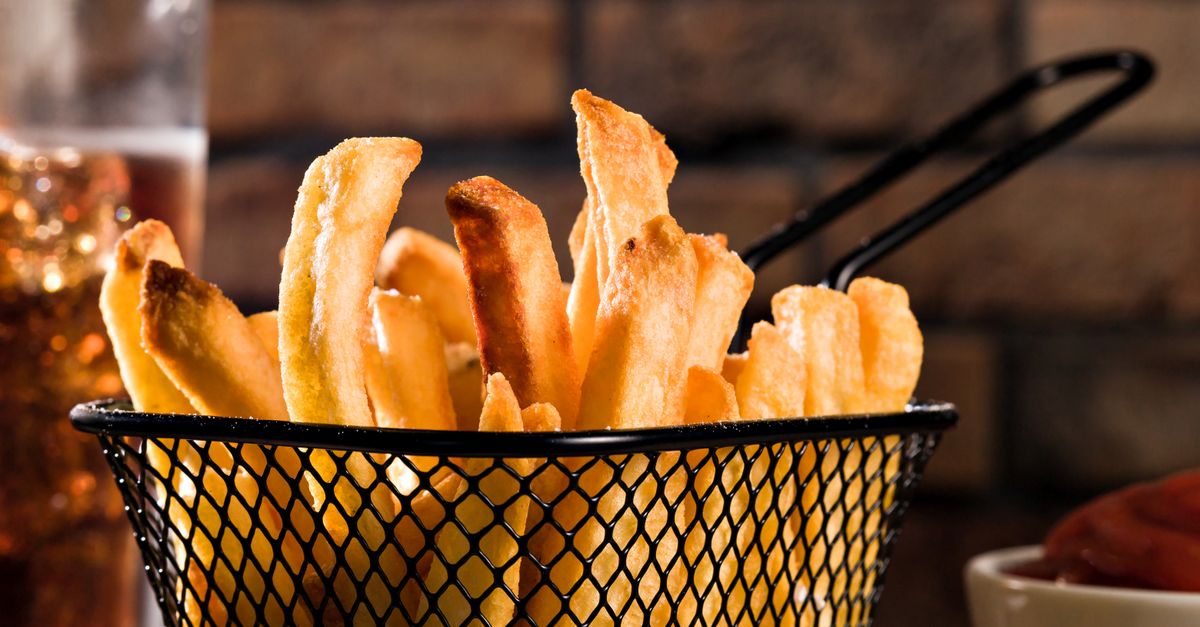 Close-up apetitoso de batatas fritas douradas em uma cesta de metal estilosa, perfeita para amantes da culinária.