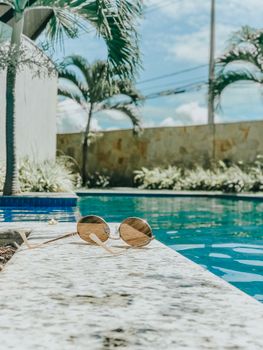 Elegant sunglasses resting on the edge of a serene pool, evoking a perfect summer vibe.