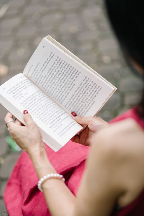 Free Close-up of a woman reading a book outdoors, focusing on hands and book detail. Stock Photo
