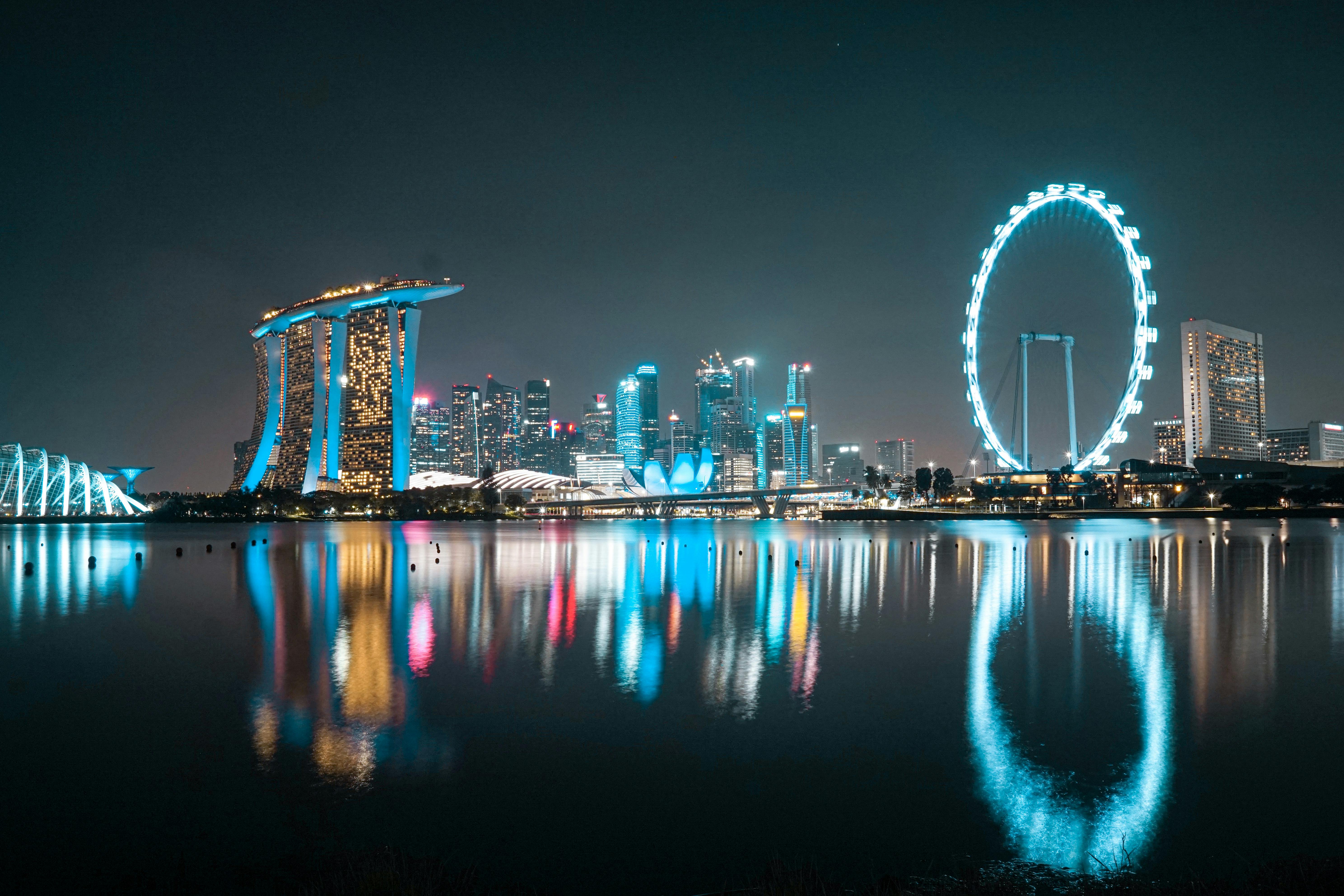 Beautiful night view of Singapore's Marina Bay skyline with illuminated Ferris wheel and reflections.