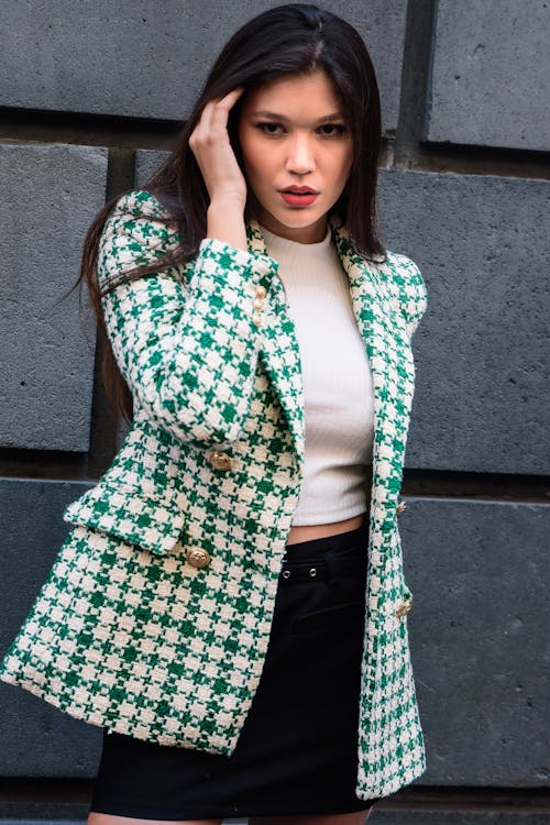 Woman in Green and White Checkered Coat Standing Beside Concrete Wall