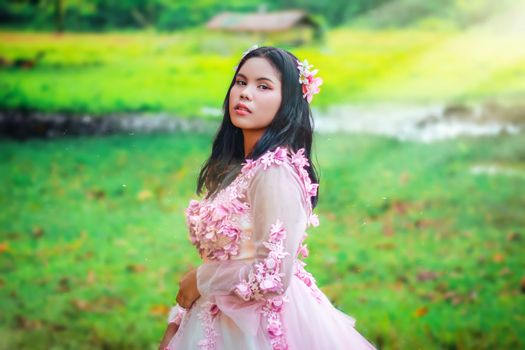 Elegant woman posing outdoors in a floral pink dress with a blurred green background.