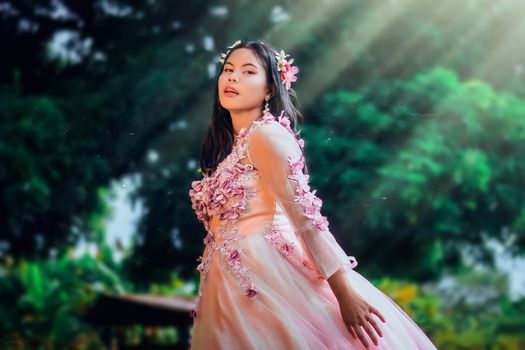 Elegant portrait of a woman in a floral embroidered gown, posing in a nature setting.