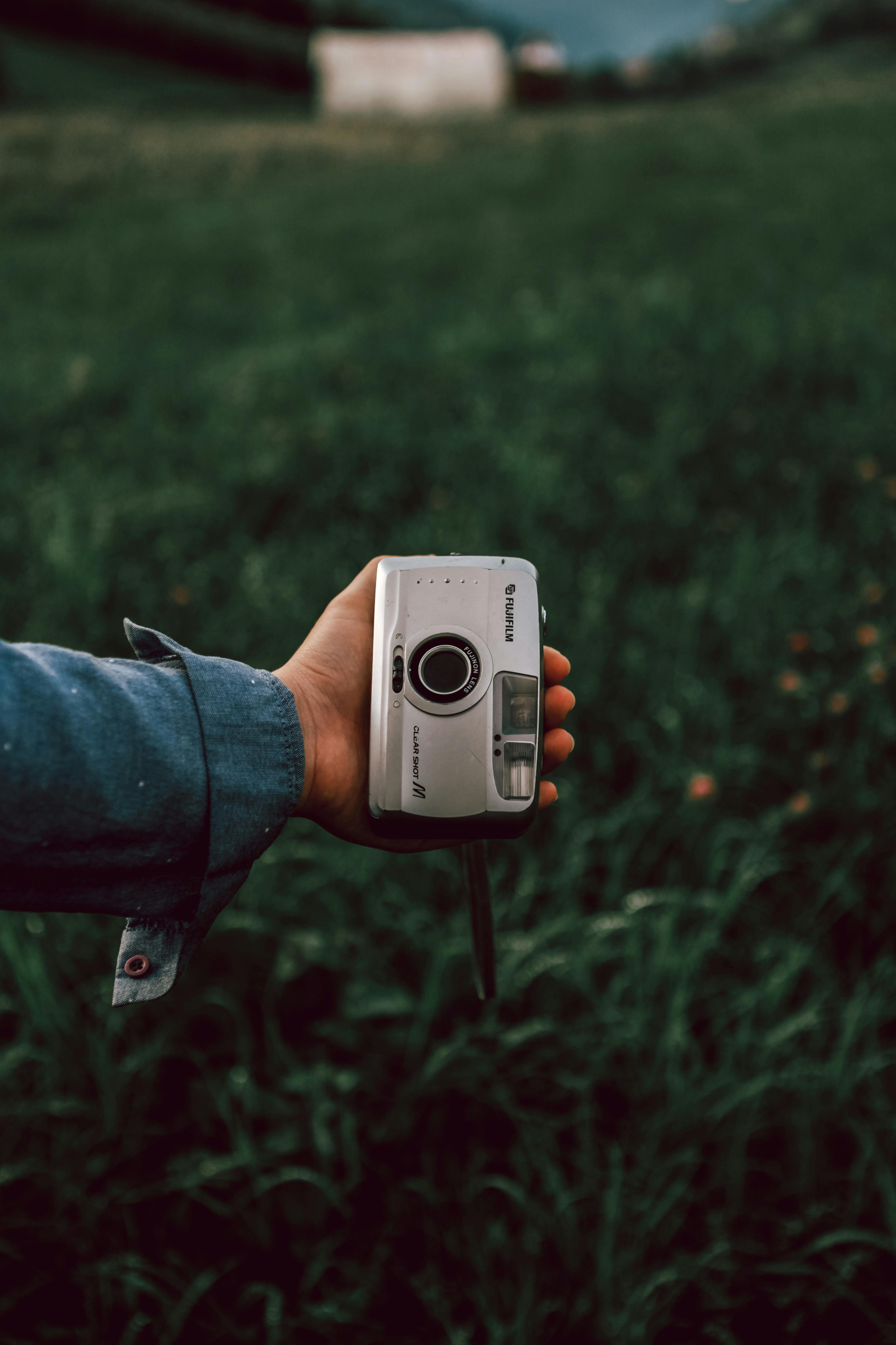 Close-up of a hand holding a vintage camera in a green field, conveying nostalgia.