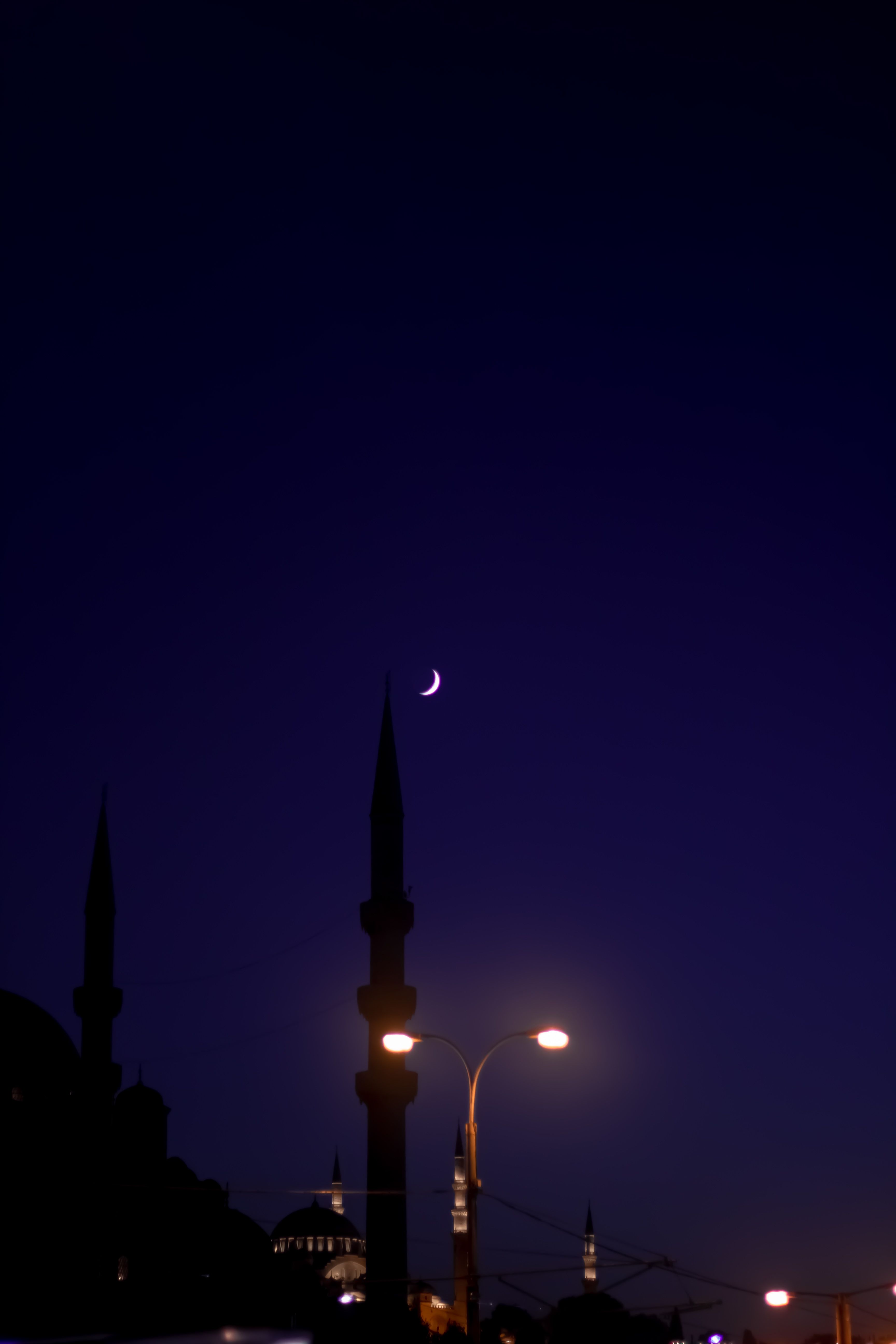 Majestic crescent moon above Istanbul's mosque minarets illuminated by street lights at night.