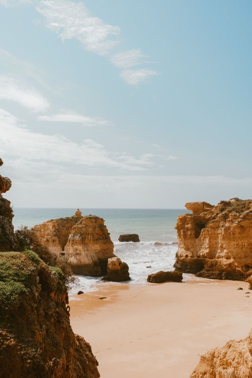 Free Peaceful sandy beach surrounded by stunning rocky cliffs and gentle ocean waves under a clear blue sky. Stock Photo
