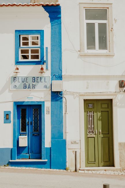 Vibrant blue and green doors of the Blue Bell Bar under bright summer daylight.