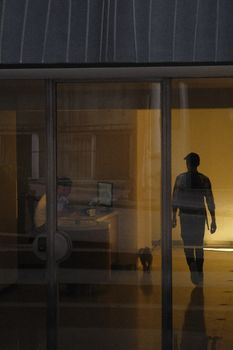 Dramatic silhouette of person walking past an office glass window with a reflection, creating a moody atmosphere.