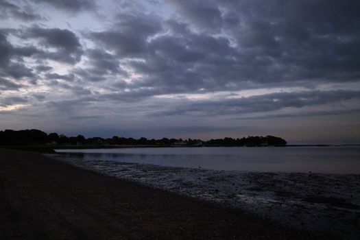 A serene twilight coastal scene with a cloudy sky over Stamford, CT shoreline reflecting the ocean.