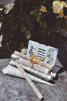 A collection of rolled music sheets with an open book featuring musical notes, set outdoors.