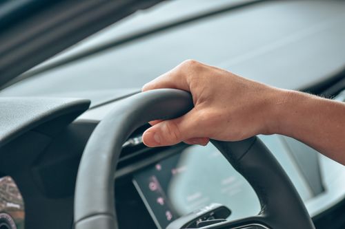 Free A close-up shot of a hand gripping a steering wheel in a modern car interior. Stock Photo
