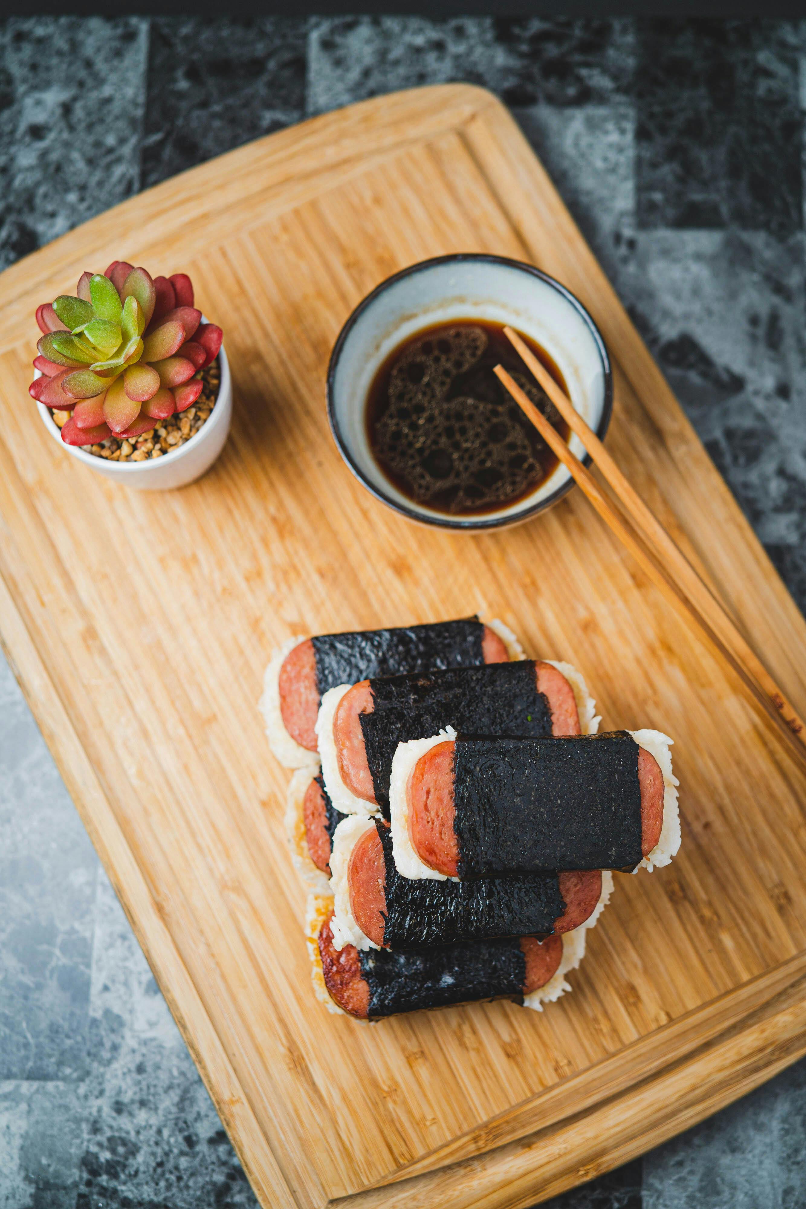 Appetizing spam musubi served with soy sauce on bamboo cutting board. Perfect for lunch delight.
