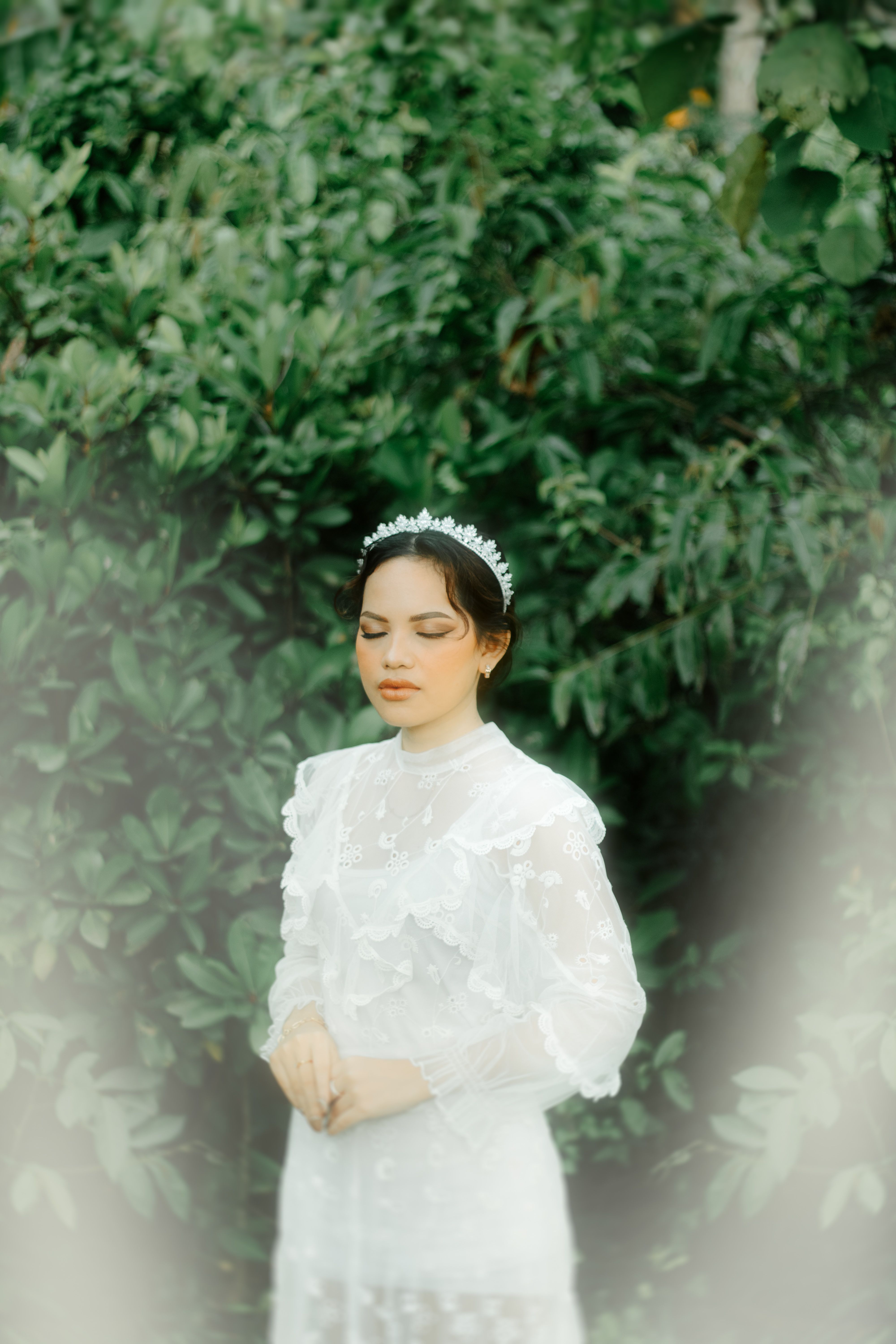 Serene portrait of an elegant woman in a white dress with closed eyes, surrounded by lush greenery.