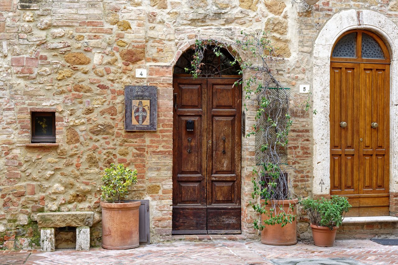 rustic wooden doors with potted plants on a stone facade in pienza tus